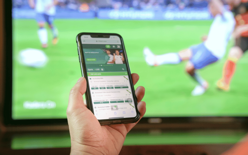 photo of phone on a iGaming platform with a football game on a TV in the background